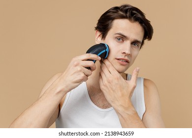 Young Fun Man He 20s Perfect Skin In Undershirt Hold Electric Razor Shaving Trimming Stubble Isolated On Pastel Light Beige Background Studio Portrait. Skin Care Healthcare Cosmetic Procedures Concept