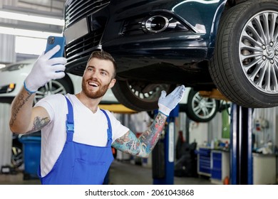 Young Fun Professional Technician Mechanic Man In Blue Overalls T-shirt Do Selfie Shot On Mobile Cell Phone Stand Near Car Lift Check Technical Condition Work In Vehicle Repair Shop Workshop Indoors