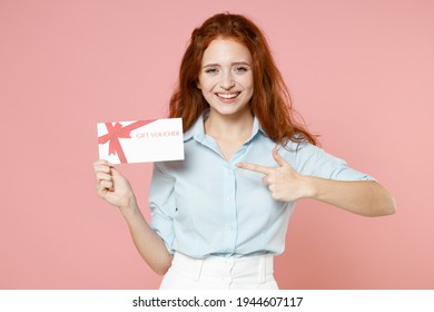 Young Fun Satisfied Smiling Happy Caucasain Ginger Student Redhead Woman 20s Wear Blue Shirt Point Index Finger On Gift Voucher Flyer Mock Up Isolated On Pastel Pink Color Background Studio Portrait