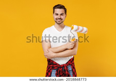 Young fun smiling employee handyman man wear t-shirt holding paint roller hands crossed isolated on yellow background studio. Instruments accessories for renovation apartment room. Repair home concept