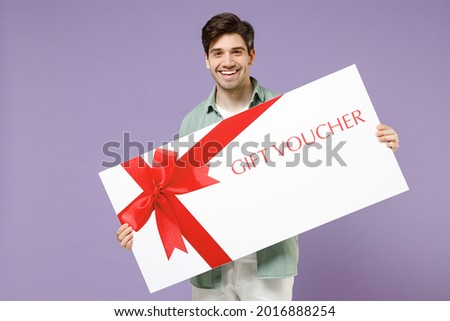 Young fun smiling excited happy caucasian man 20s wearing casual mint shirt white t-shirt hold big gift voucher flyer mock up isolated on purple background studio portrait People lifestyle concept.