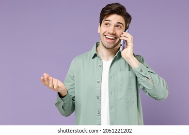 Young Fun Smiling Happy Caucasian Man 20s Wear Casual Mint Shirt White T-shirt Talking Speaking By Mobile Cell Phone Spread Hand Isolated On Purple Background Studio Portrait People Lifestyle Concept