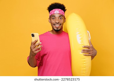 Young fun smiling happy cheerful man 20s he wear pink t-shirt near hotel pool hold in hand inflatable ring use mobile cell phone isolated on plain yellow background. Summer vacation sea rest concept - Shutterstock ID 2278523175