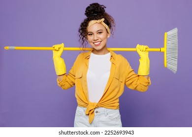 Young fun smiling happy housekeeper woman wear yellow shirt tidy up hold broom behind herself sweeps floor clean house isolated on plain pastel purple background studio. Housework housekeeping concept - Shutterstock ID 2252693943