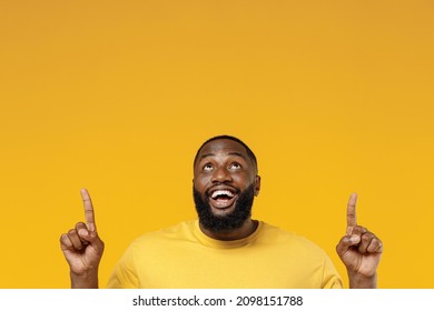 Young Fun Smiling Happy Man Of African American Ethnicity 20s Wear Bright Casual T-shirt Point Index Finger Overhead On Workspace Area Mock Up Isolated On Plain Yellow Color Background Studio Portrait