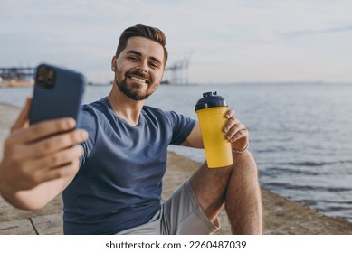 Young fun sporty strong sportsman man in sports clothes shorts train do selfie shot photo on mobile cell phone drink water at sunrise sun over sea beach outdoor on pier seaside in summer day morning - Powered by Shutterstock