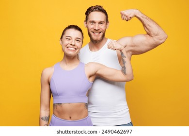 Young fun strong fitness trainer instructor sporty two man woman wear blue clothes spend time in home gym showing biceps muscles on hand isolated on plain yellow background. Workout sport fit concept - Powered by Shutterstock