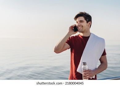 Young Fun Strong Sporty Athletic Fit Sportsman Man In Sports Clothes Towel Speak Talk On Mobile Cell Phone Water Warm Up Training At Sunrise Sun Dawn Over Sea Beach Outdoor On Pier Seaside In Morning