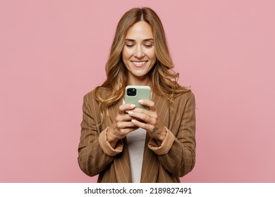 Young Fun Successful Employee Business Woman 30s She Wearing Casual Brown Classic Jacket Hold In Hand Use Mobile Cell Phone In Green Case Isolated On Plain Pastel Light Pink Background Studio Portrait