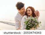 Young fun surprised couple family man woman in white clothes rest relax together boyfriend meet girlfriend close eyes gift give bouquet flowers at sunrise over sea beach outdoor seaside in summer day