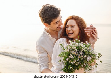 Young fun surprised couple family man woman in white clothes rest relax together boyfriend meet girlfriend close eyes gift give bouquet flowers at sunrise over sea beach outdoor seaside in summer day - Shutterstock ID 2053474343