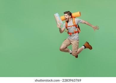 Young fun surprised traveler white man carry backpack stuff mat hold map jump isolated on plain green background Tourist leads active lifestyle walk on spare time. Hiking trek rest travel trip concept