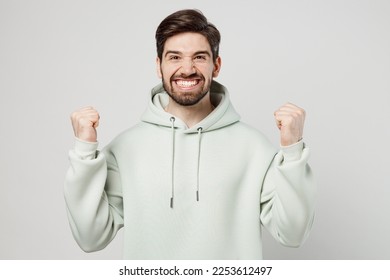 Young fun unshaven caucasian man wear mint hoody look camera doing winner gesture celebrate clenching fists say yes isolated on plain solid white background studio portrait. People lifestyle concept - Shutterstock ID 2253612497