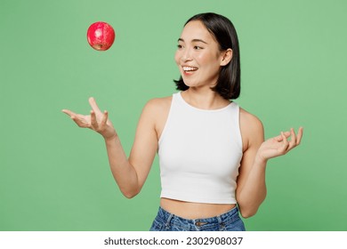 Young fun vegetarian woman wear white clothe hold in hand toss up ripe red apple playing isolated on plain pastel light green background. Proper nutrition healthy fast food unhealthy choice concept