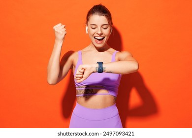 Young fun winner fitness trainer instructor woman sportsman wear purple top clothes smartwatch in home gym listen music in earphones isolated on plain orange background. Workout sport fit abs concept - Powered by Shutterstock