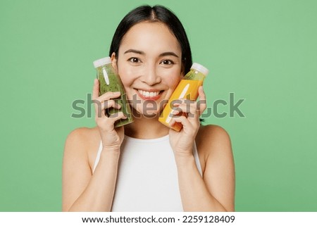 Young fun woan wear white clothes hold fruit juice yellow vegetable smoothie as detox diet isolated on plain pastel light green background. Proper nutrition healthy fast food unhealthy choice concept