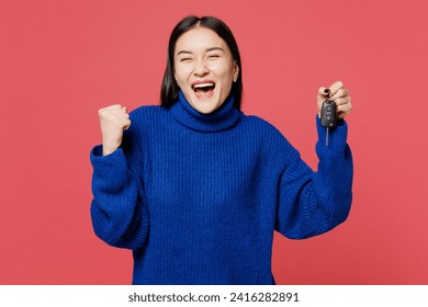 Young fun woman of Asian ethnicity she wear blue sweater casual clothes hold key fob keyless system do winner gesture isolated on plain pastel light pink background studio portrait. Lifestyle concept