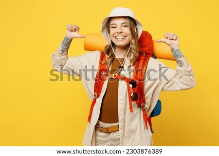 Young fun woman carry backpack with stuff mat point thumb finger on herself isolated on plain yellow background. Tourist leads active lifestyle walk on spare time. Hiking trek rest travel trip concept