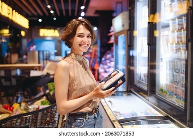 Young fun woman in casual clothes shopping at supermaket grocery store buy choose products stand near refrigerator hold container read ingredients shelf life inside hypermarket Purchasing food concept