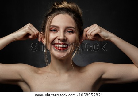young fun woman on black background, shows her ears, grimacing