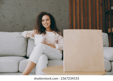 Young fun woman wear casual clothes sit on grey sofa couch eat Chinese food cuisine blank takeaway carton container box stay at home hotel flat rest relax spend free spare time in living room indoor - Shutterstock ID 2367234533