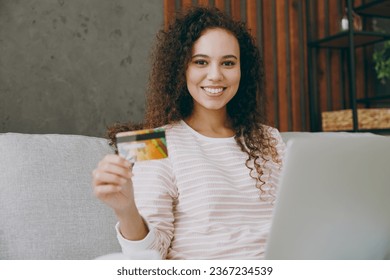 Young fun woman wear casual clothes sits on grey sofa couch hold credit bank card use laptop pc computer shopping online stay at home hotel flat rest relax spend free spare time in living room indoor - Shutterstock ID 2367234539