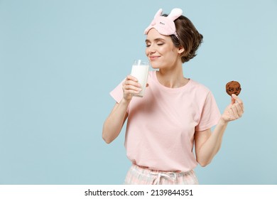 Young fun woman wear pajamas jam sleep eye mask rest relaxing at home hold glass of milk drink keep sweet cookie isolated on pastel blue background studio. Breakfast lifestyle night bedtime concept