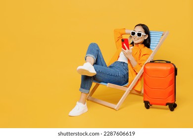 Young fun woman wear summer clothes sit in deckchair use mobile cell phone isolated on plain yellow background. Tourist travel abroad in free spare time rest getaway. Air flight trip journey concept - Shutterstock ID 2287606619