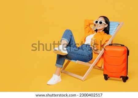 Young fun woman wear summer clothes sit in deckchair hold hand behind neck isolated on plain yellow background. Tourist travel abroad in free spare time rest getaway. Air flight trip journey concept