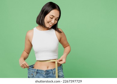 Young fun woman wear white clothes show loose pants after weightloss hold measure tape on waist isolated on plain pastel green background. Proper nutrition healthy fast food unhealthy choice concept - Powered by Shutterstock