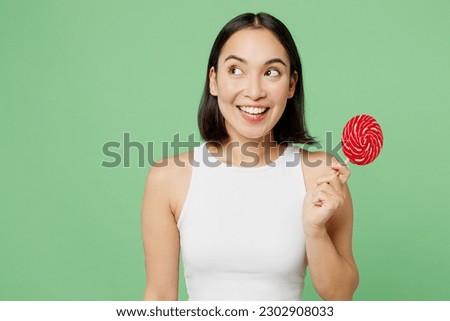 Young fun woman wear white clothes hold cover mouth with round lollipop look aside on area isolated on plain pastel light green background. Proper nutrition healthy fast food unhealthy choice concept