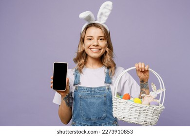 Young fun woman wearing casual clothes bunny rabbit ears hold wicker basket colorful eggs use blank screen mobile cell phone isolated on plain purple background studio portrait. Happy Easter concept - Powered by Shutterstock