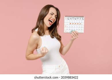 Young fun woman in white clothes hold female periods calendar for checking menstruation days do winner gesture scream yes isolated on pastel pink background Medical healthcare gynecological concept.