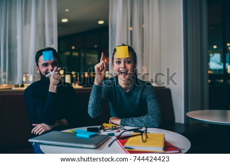Young funny best friends dressed in trendy clothing enjoying leisure game indoors and fooling each other.Portrait of happy girl emotionally showing she's got idea while bearded man laughing with her