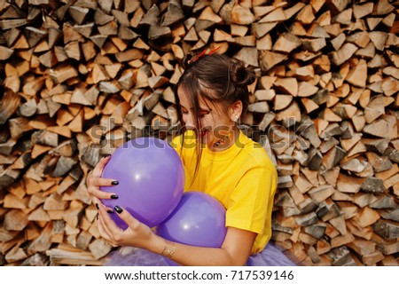 Young funny girl with bright make-up, wear on yellow shirt with colored balloons against wooden background.