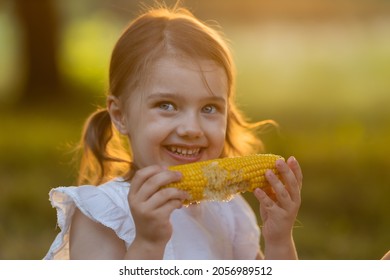 Young Funny Girl Eating A Boiled Corn. Child In The Garden, Girl Eating Corn On The Cob, GMO Free Food. Kids Eat Fruit Outdoors. Healthy Snack For Children. Summer Concept. High Quality Photo