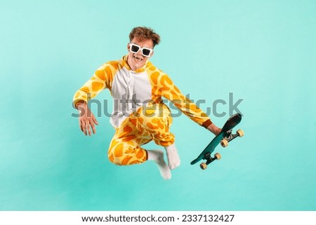 young funny guy in orange giraffe pajamas jumps and flies with skateboard on blue isolated background, man in animal costume does extreme trick in the air, pajama disco concept