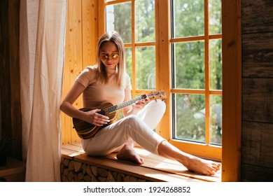 Young Funny Hipster Girl Having Fun And Playing On Small Ukulele Guitar In A Cabin, Positive Mood. Instagram Live Concert