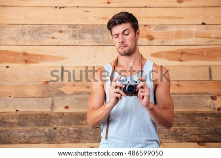Young funny man taking photo with old vintage photo camera over wooden background