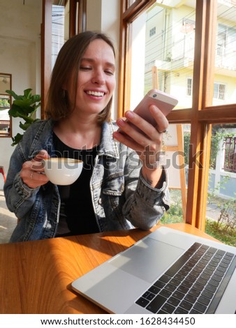 Young funny tattooed freelance girl texting mesage on her phone and drinking coffee.