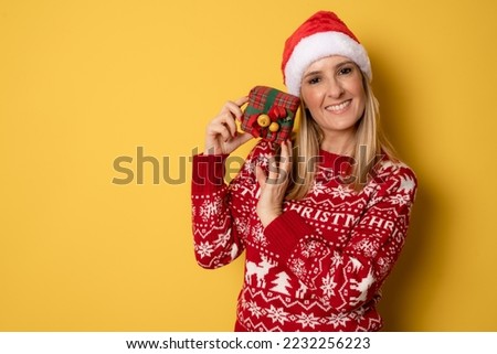 Young funny woman lady wear knitted jumper and santa hat holding gift box isolated yellow background