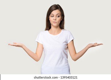 Young funny woman wearing white t-shirt stretched hands feels confused pose isolated on grey wall, girl imagining alternatives, weighs pros and cons, choosing make not easy difficult decision concept - Shutterstock ID 1395403121