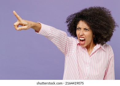 Young furious angry sad indignant woman of African American ethnicity 20s wearing pink striped shirt point index finger aside scream isolated on plain pastel light purple background studio portrait