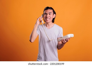 Young Furious Man Talking On Landline Phone, Shouting. Angry Asian Teenager Screaming, Holding Retro Telephone, Person With Aggressive Facial Expression Standing, Having Conversation