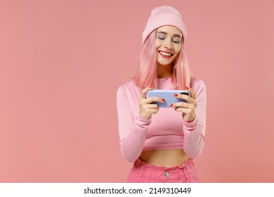 Young Gambling Fun Woman With Dyed Rose Hair In Rosy Top Shirt Hat Using Play Racing App On Mobile Cell Phone Hold Gadget Smartphone For Pc Video Games Isolated On Plain Light Pastel Pink Background