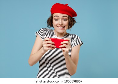 Young Gambling Woman, Short Hairdo In French Beret Red Hat Striped T-shirt Using Play Racing On Mobile Cell Phone Hold Gadget Smartphone For Pc Video Games Isolated On Pastel Blue Background Studio