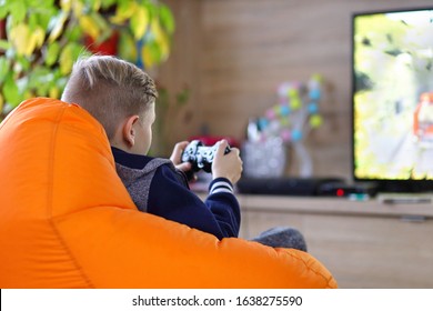 Young Gamer Boy Playing Online Car Racing Game On New Console At Home Tv – Little Kid Sitting In Gamer Bean Bag Chair Having Fun Streaming Online – New Technology Game Trends And Entertainment Concept