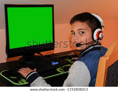 A young gamer boy playing video games on computer wearing headphones and colorful keyboard