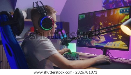 Young gamer in headphones talks with teammates and plays in third person shooter on computer at home. Online video game live streaming or esports competition. Concept of multiplayer PvP on home PC.