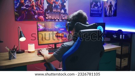 Young gamer plays in car racing simulator on PC at home. Computer monitor with displayed online video game live stream or cybersport championship. Desk illuminated by RGB LED strip light.